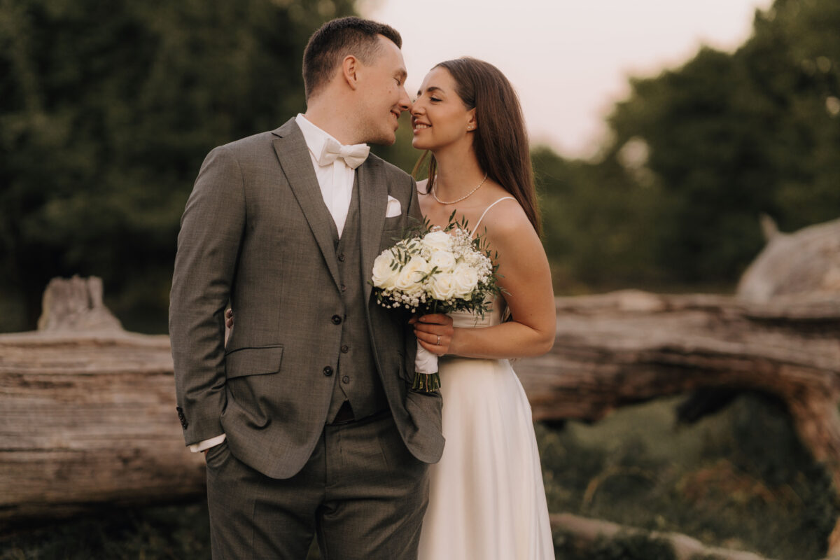 After Wedding Portfolio, Braut steht an der Seite des Bräutigams, sie haben ihre Nasenspitzen nah beieinander und das Licht ist leicht rötlich durch die untergehende Sonne