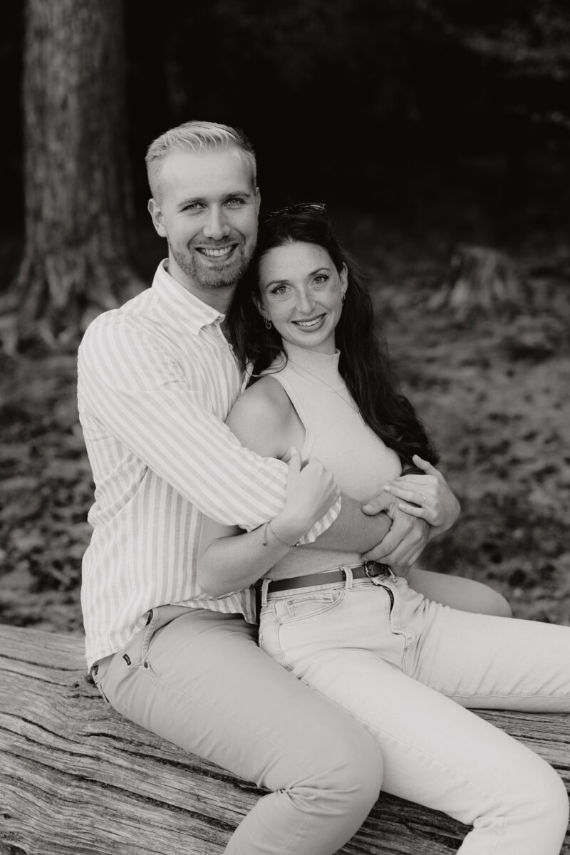 Paar sitzt Arm in Arm auf einer Decke und lächelt in die Kamera, fotografiert in Schwarz-Weiß