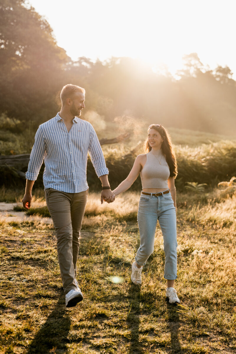 Paar schlendert in der Abendsonne über eine Wiese und schaut sich an