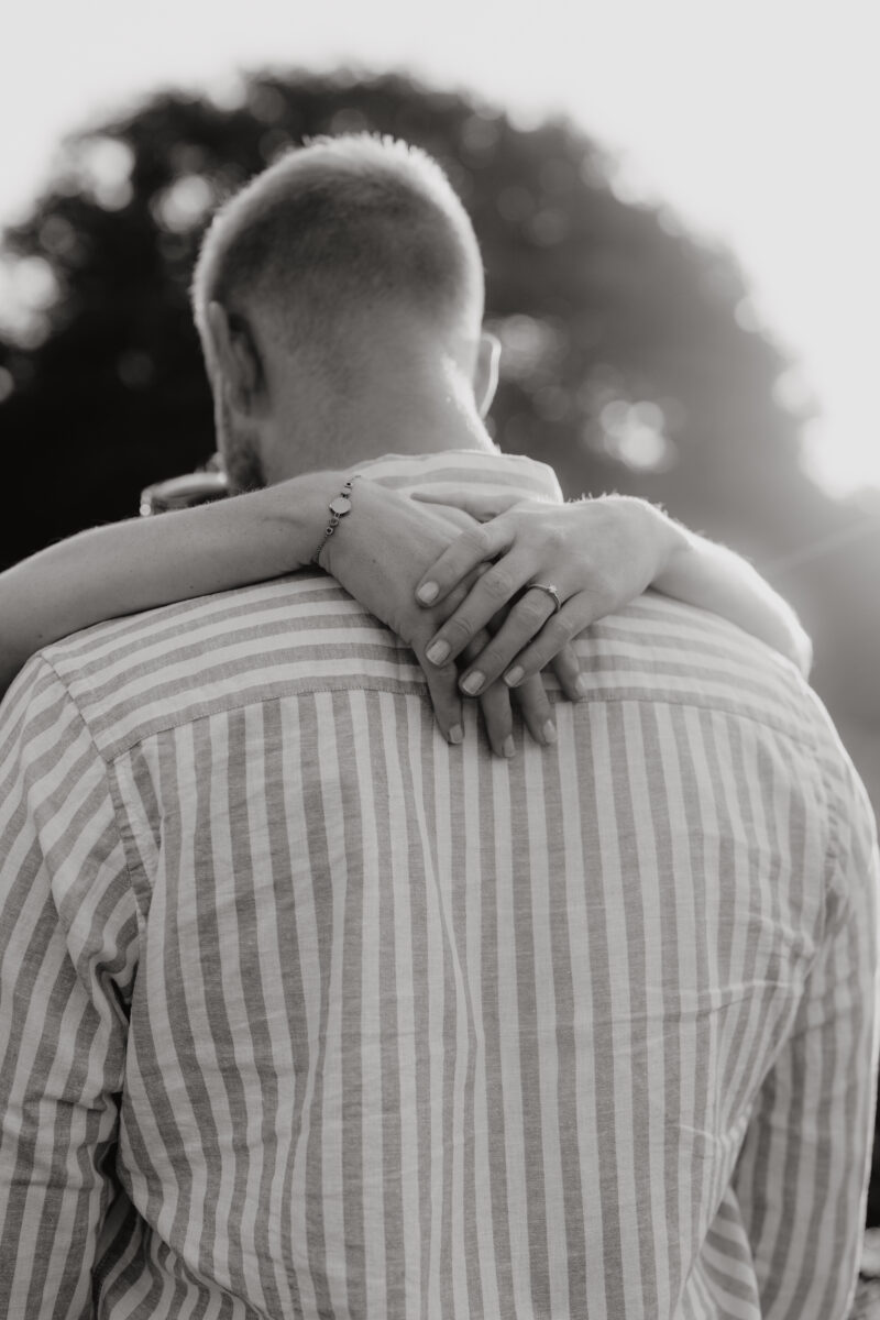 Sie umarmt ihn, Fokus auf ihre Hände auf seinem Rücken, fotografiert in Schwarz-Weiß