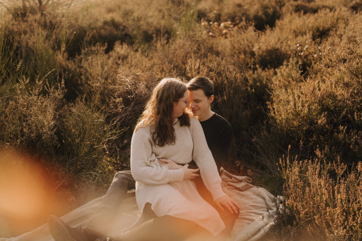 Paar sitzt in der Abendsonne auf einer Decke und setzt zum Kuss an