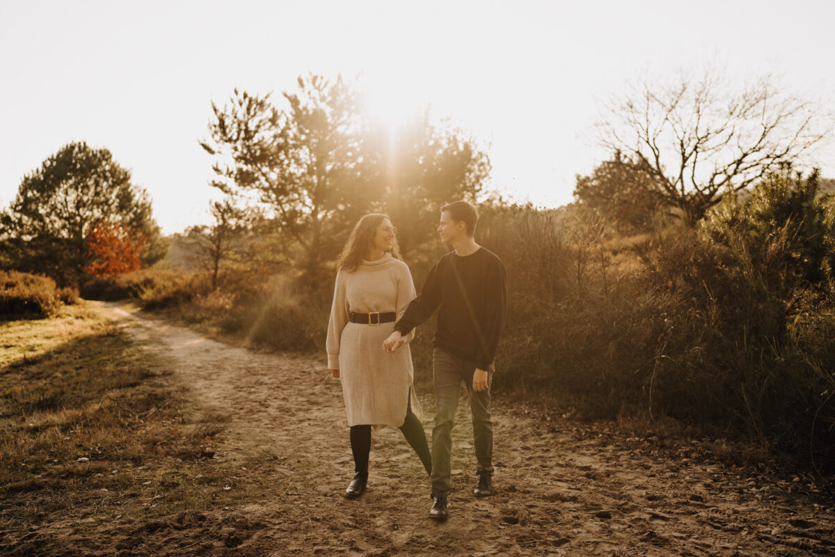 Paar schlendert im Sonnenuntergang, Händchen haltend auf die Kamera zu