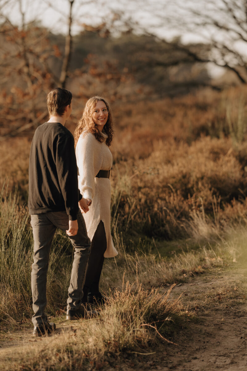Paar schlendert hintereinander auf einer Wiese und en Sonnenuntergang