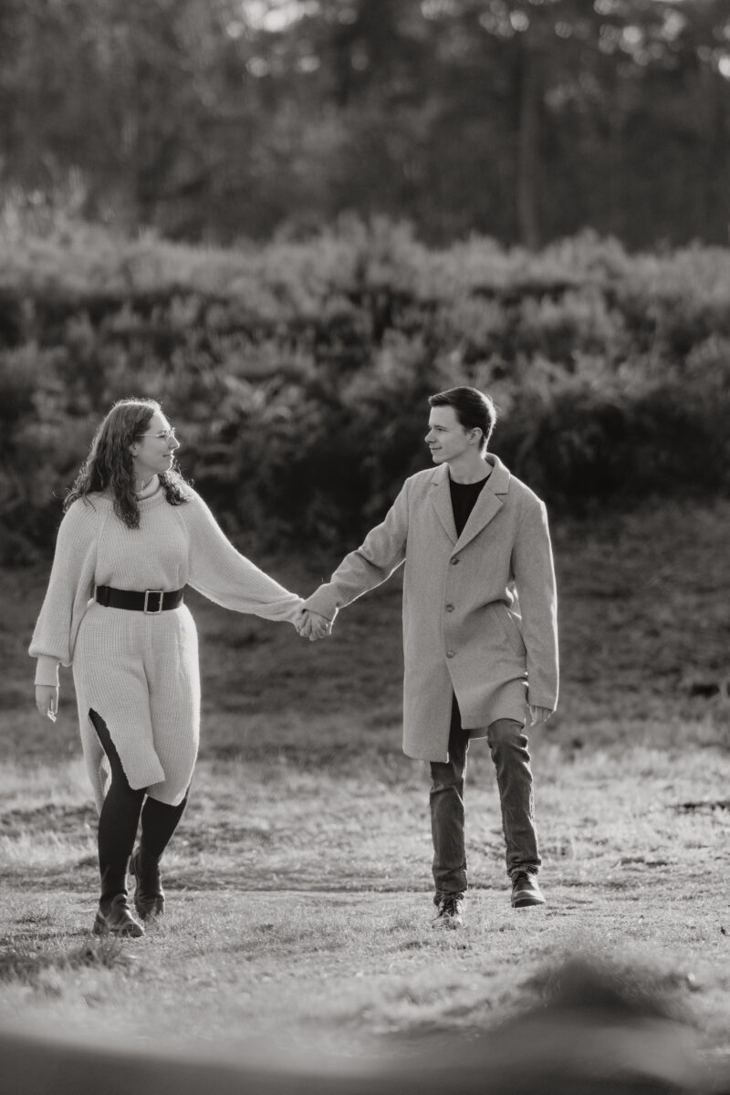 Paar schlendert Händchen haltend auf die Kamera zu, sie schauen sich an, fotografiert in Schwarz-Weiß