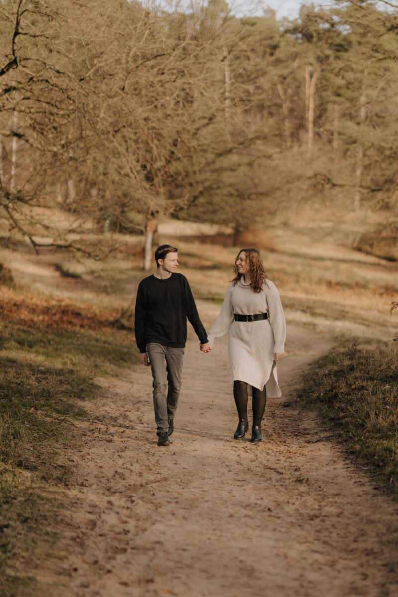 Paar schlendert Händchen haltend auf die Kamera zu, sie schauen sich an