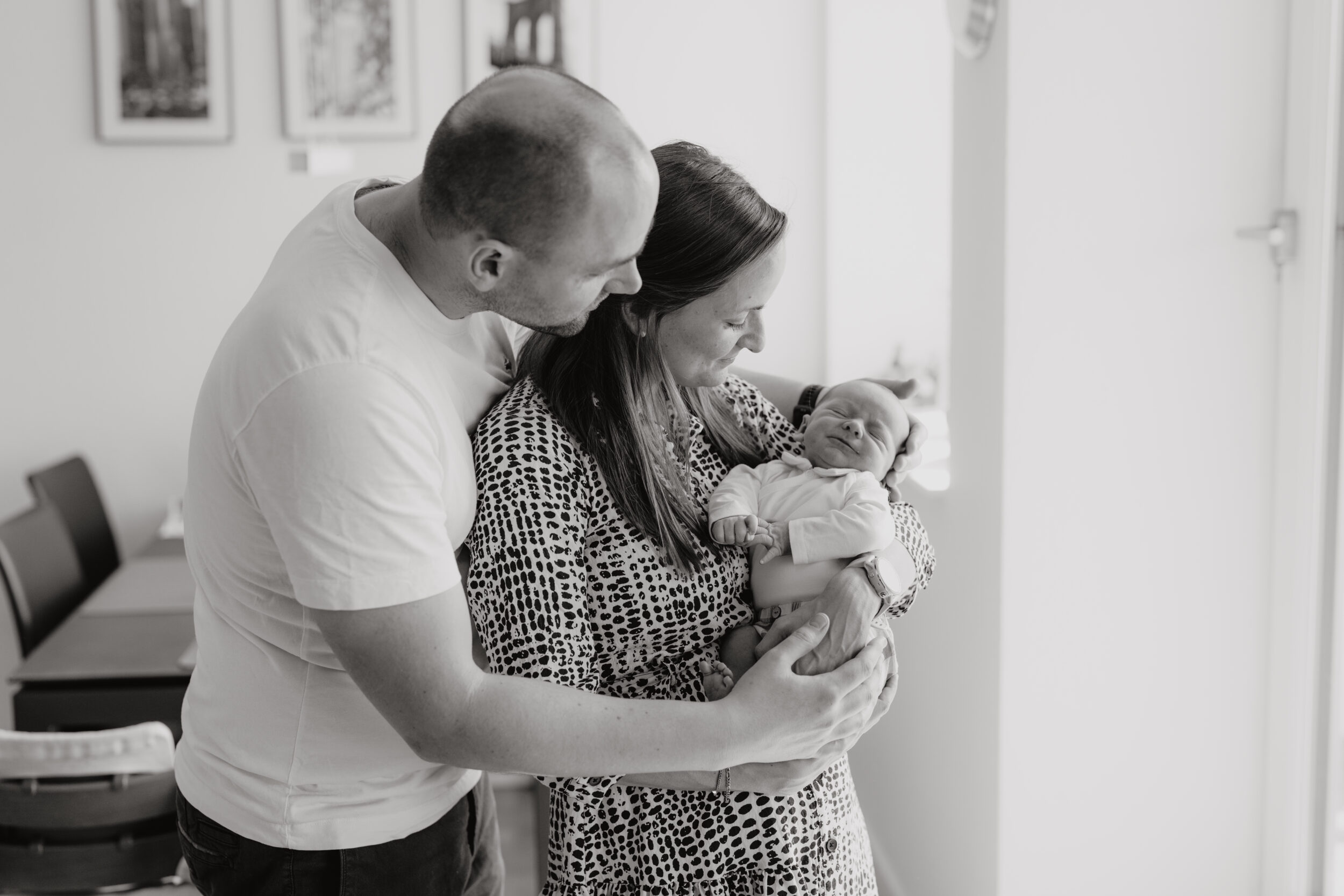 Newborn Portfolio Mama hält Baby im Arm, Papa hält Mama von hinten im Arm, schwarz-weiß