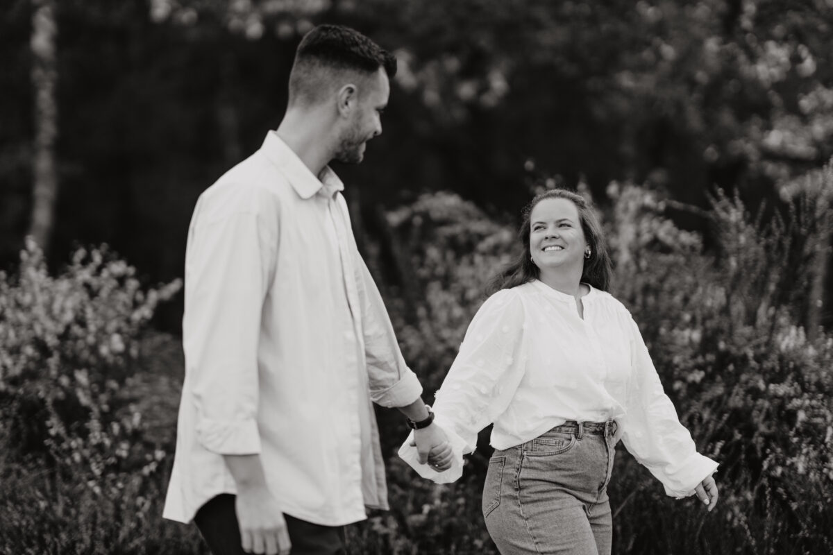 Paar schlendert Händchen haltend im Wald, fotografiert in Schwarz-Weiß