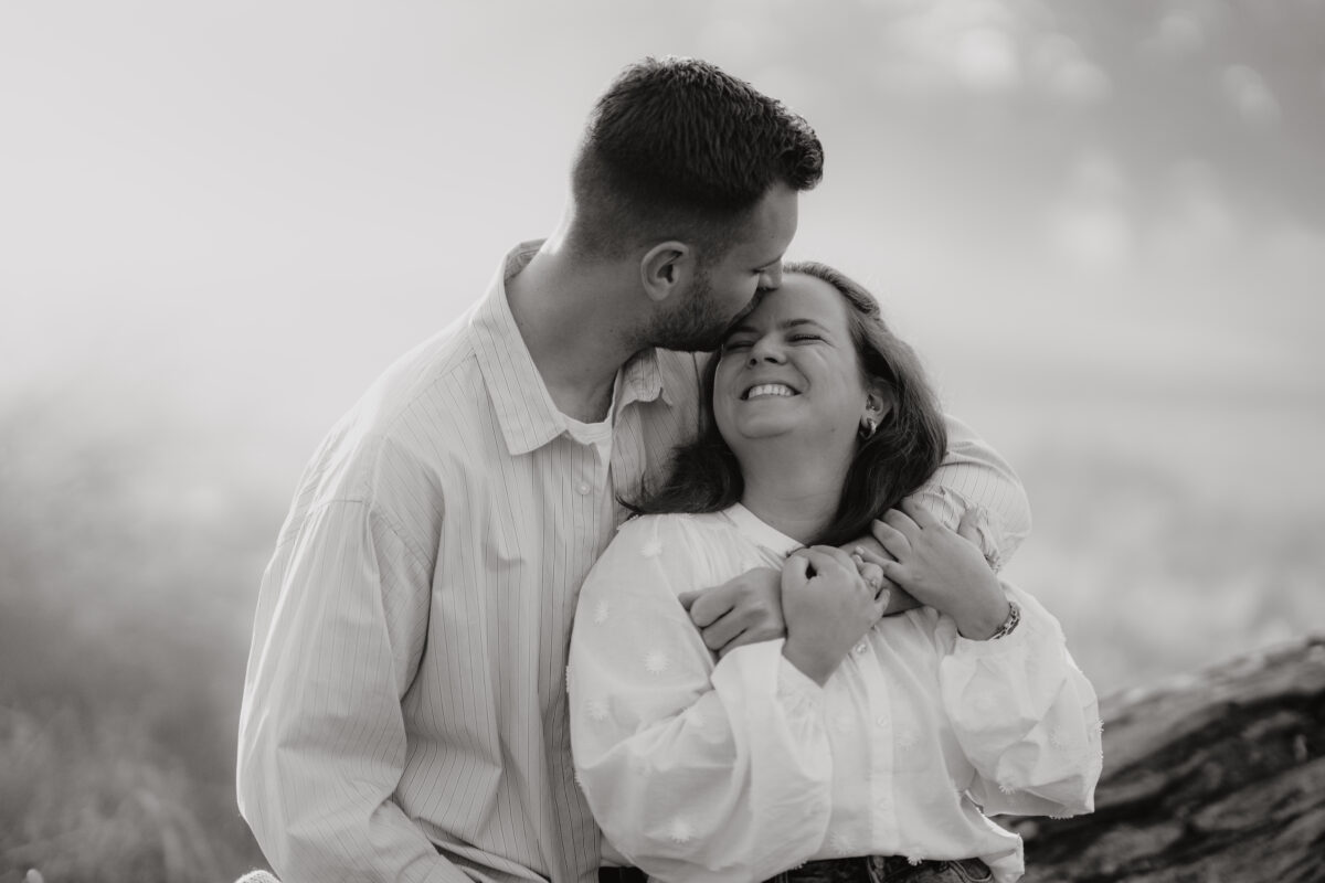 Er umarmt sie von hinten und lacht, fotografiert in Schwarz-Weiß