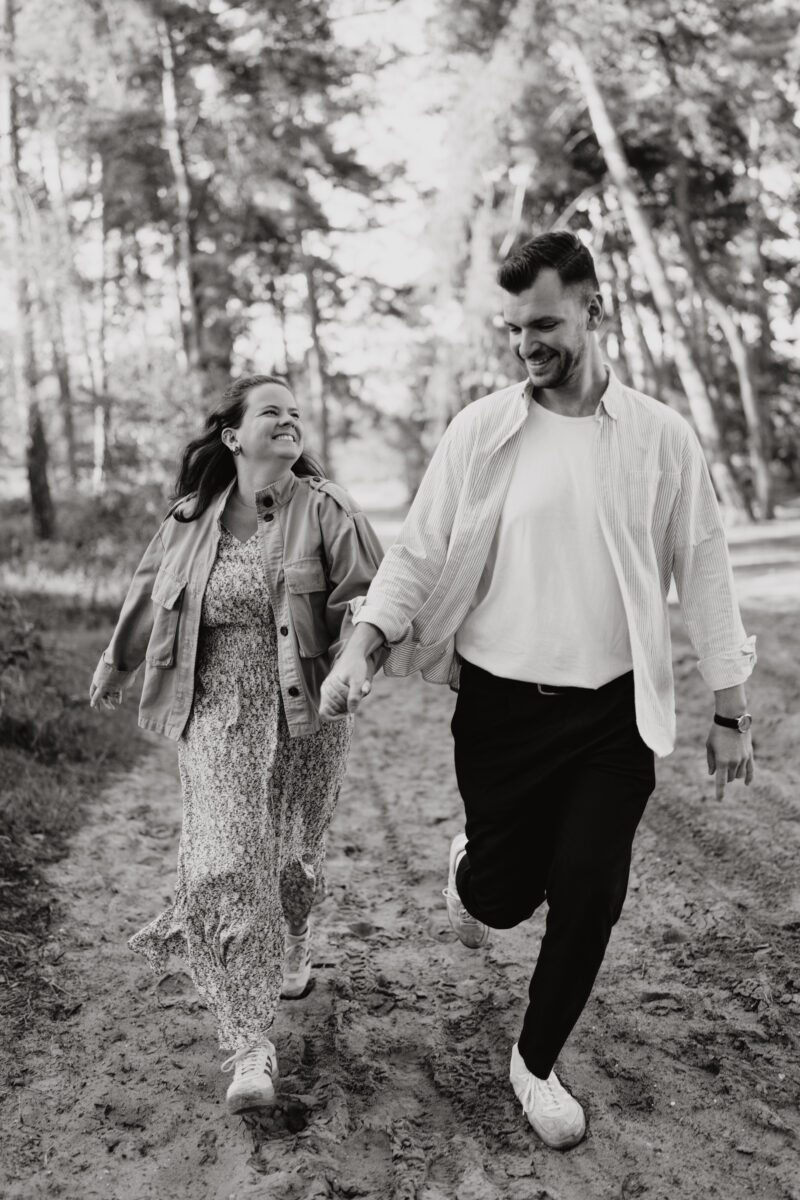 Paar läuft Händchen haltend im Wald und schaut sich an, fotografiert in Schwarz -Weiß