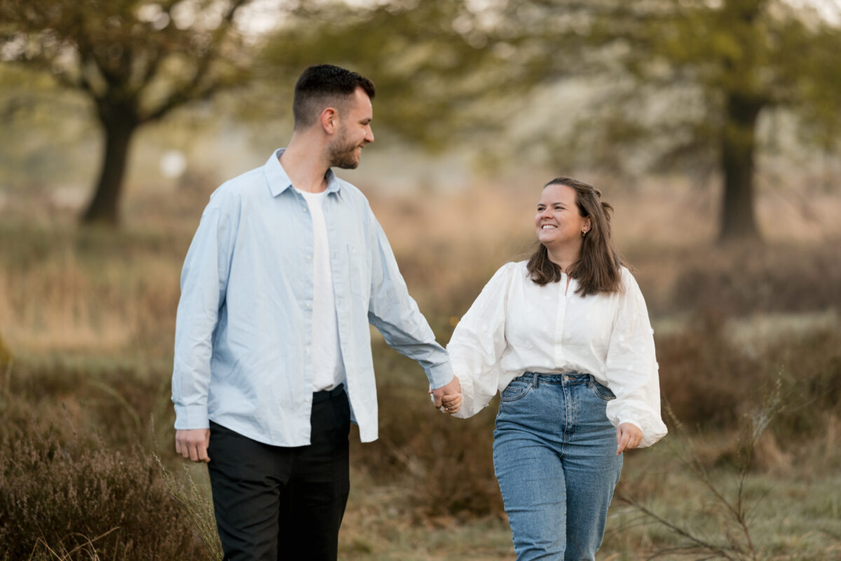 Paar schlendert Händchen haltend durch den Wald und lacht