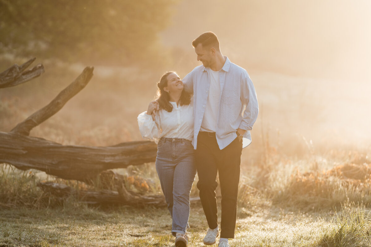 Paar geht in der Abendsonne Händchen haltend über eine Wiese und schaut sich an