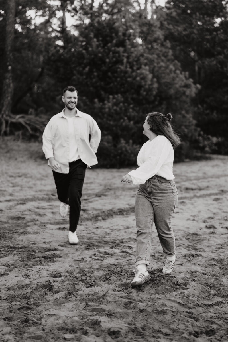 Paar läuft zusammen über eine Wiese und lacht, in Schwarz-Weiß fotografiert