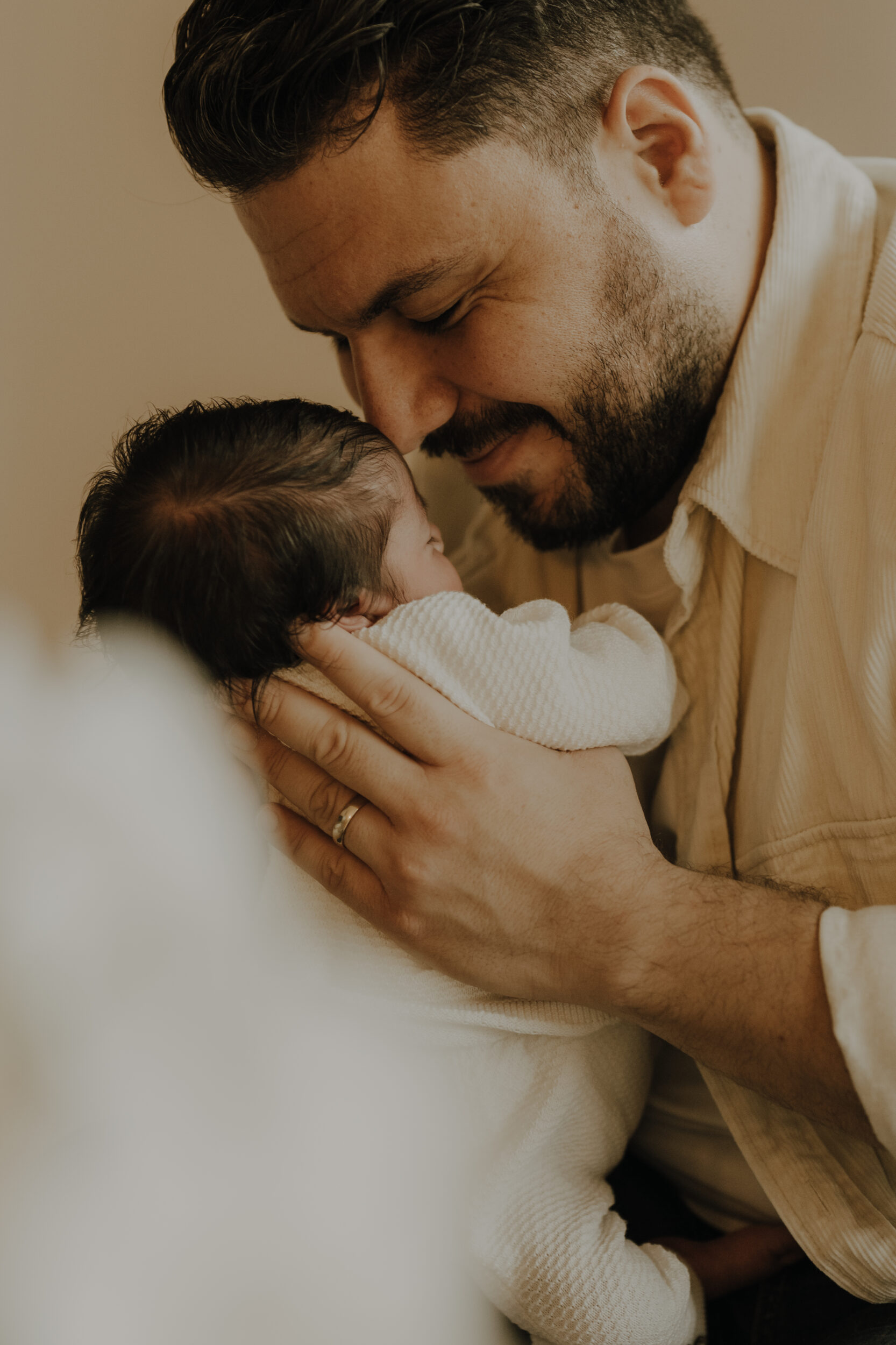 Newborn Portfolio Papa mit dunklem Bart hält Baby mit dunklem Haar an sein Gesicht