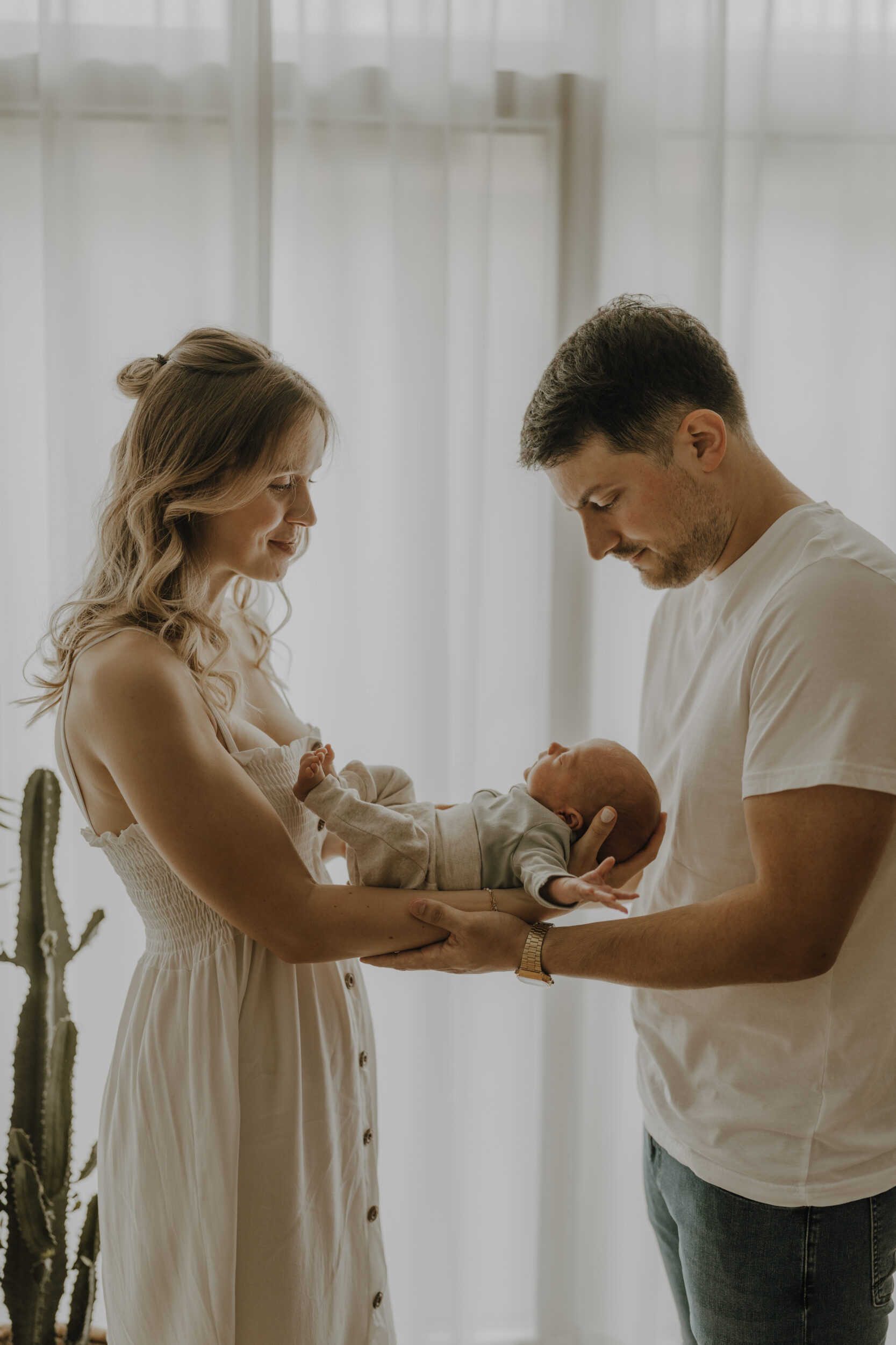Newborn Portfolio Mama und Papa stehen sich mit ausgestreckten armen gegenüber, Baby auf den Armen liegend