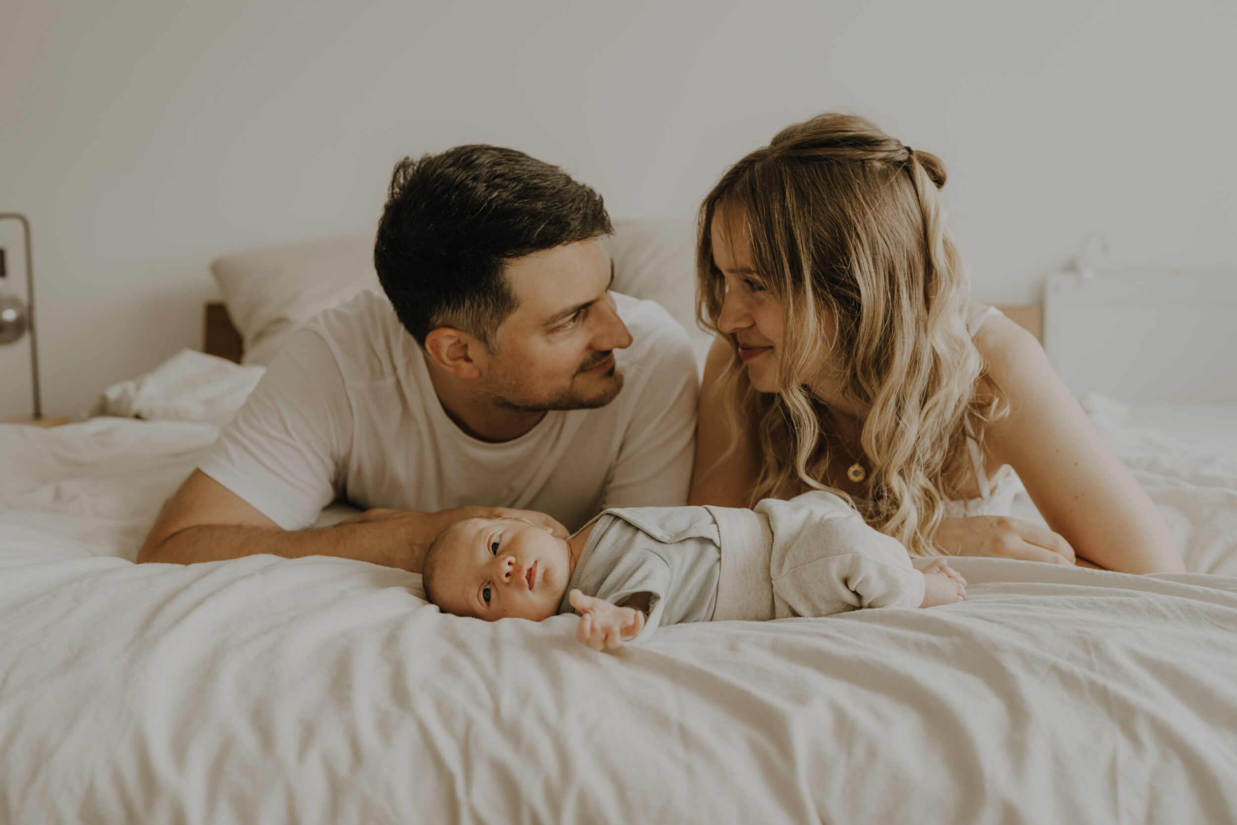 Newborn Portfolio Mama, Papa und Baby liegen auf dem Bett, Eltern schauen sich an