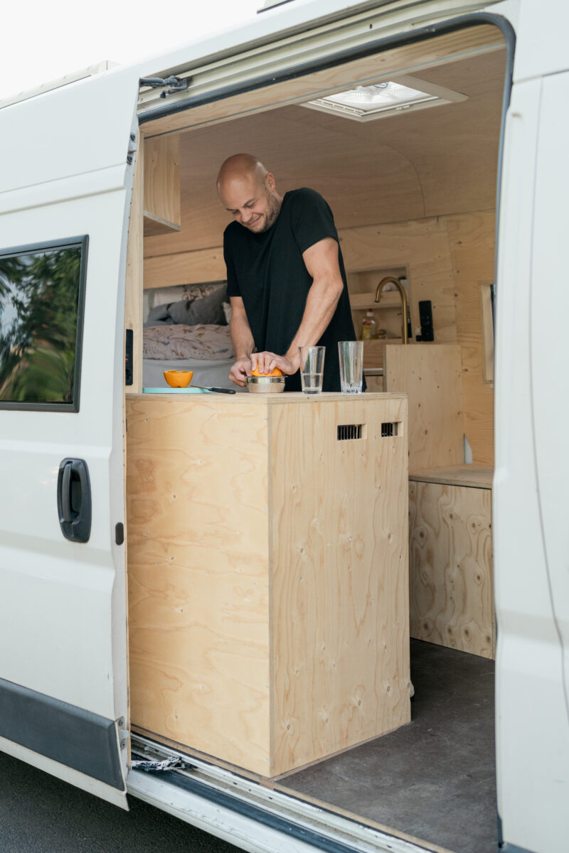 Portraitfoto eines Mannes, wie er in der Küche eines Wohnwagens Orangen auspresst