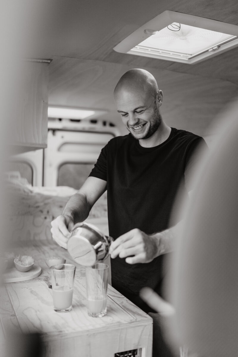 Schwarz-Weiß Portraitfoto eines Mannes wie er in der Küche Saft presst