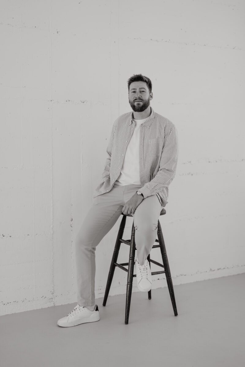 Schwarz-Weiß Portraitfoto eines Mannes, auf einem Hocker sitzend