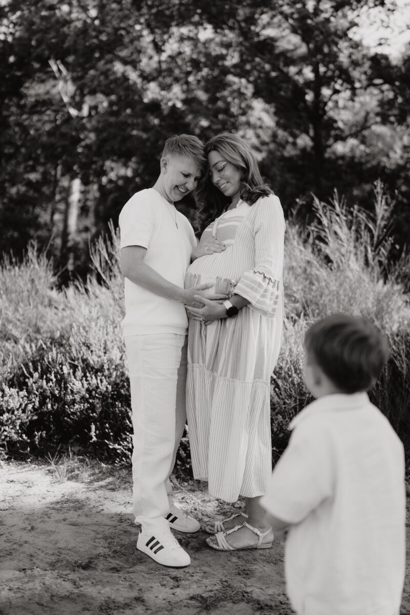 Babybauch Fotografie Portfolio werdendes Elternpaar posiert in der Natur Kleinkind kommt auf sie zu Schwarz-Weiß-Aufnahme