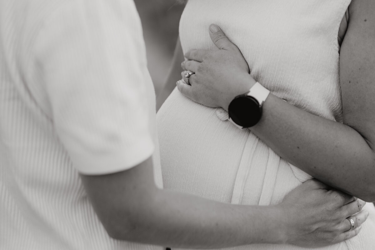 Babybauch Fotografie Portfolio Nahaufnahme vom Babybauch und den Händen der Eltern Schwarz-Weiß-Fotografie