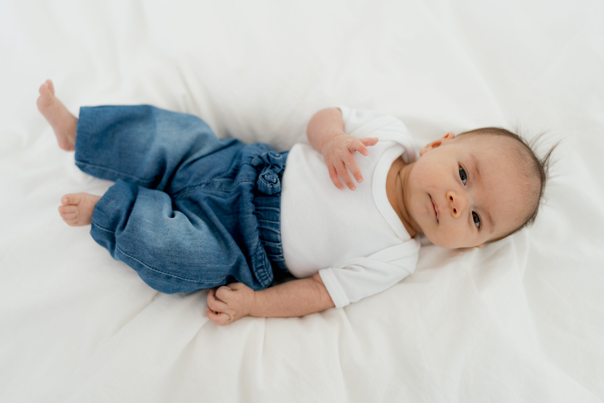Newborn Portfolio Baby auf weißer Bettdecke blaue Jeans und weißes T-Shirt