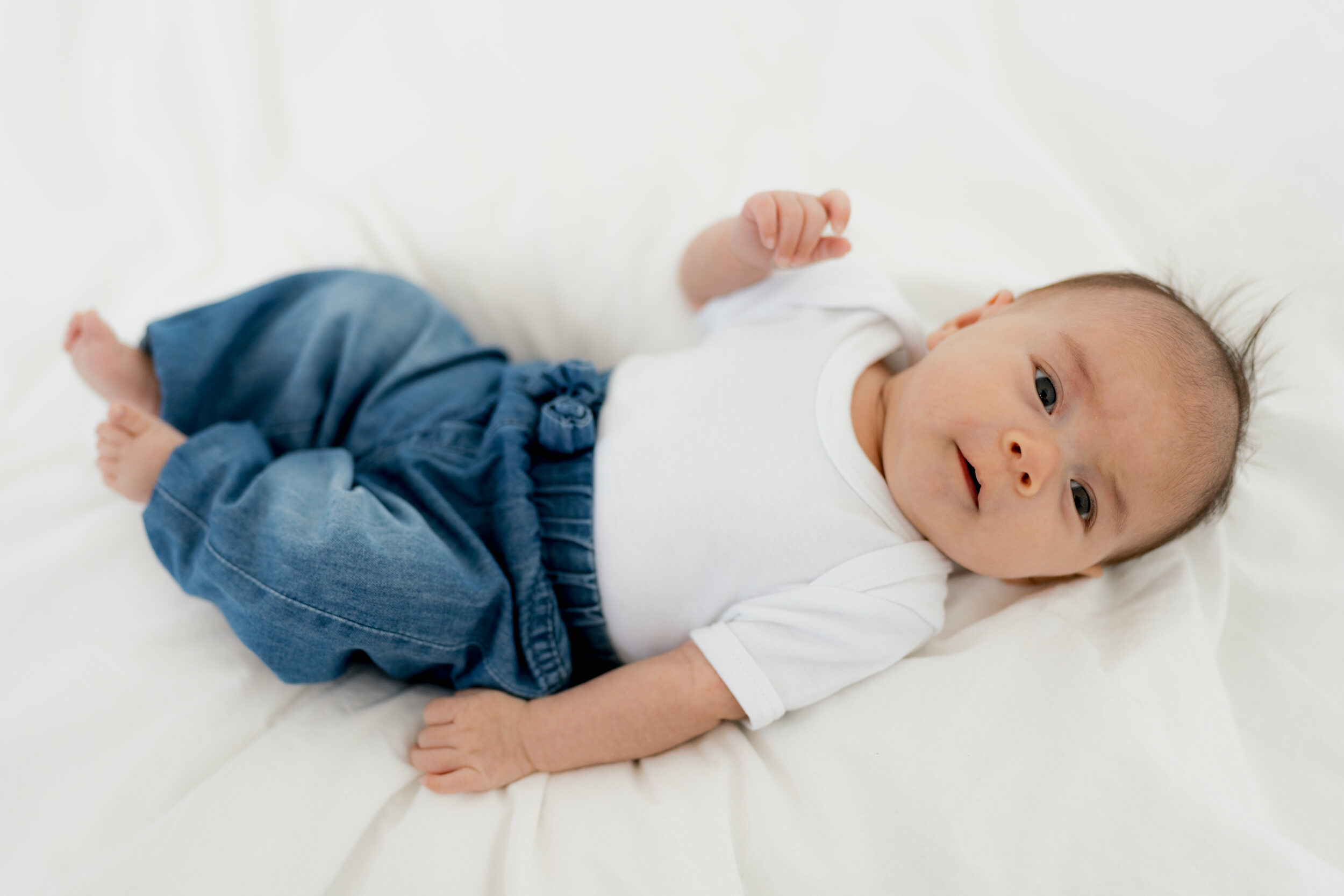 Newborn Portfolio Baby auf weißer Bettdecke, weißem T-Shirt und blauer Jeans
