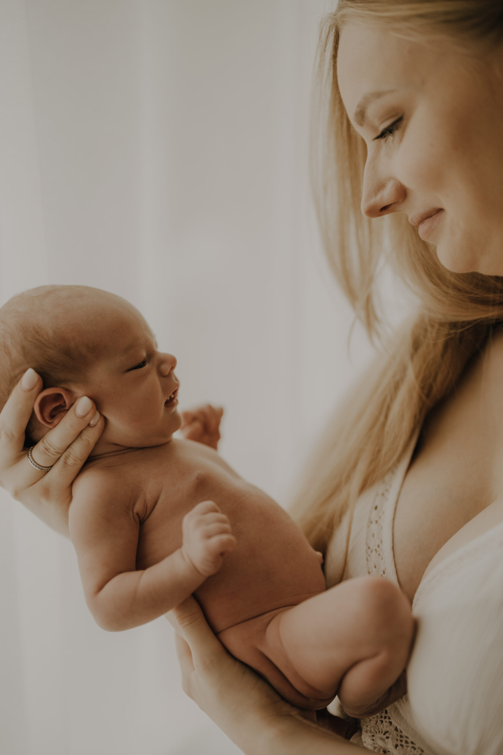 Newborn Portfolio Mama hält Säugling liebevoll im Arm und schaut ihn an