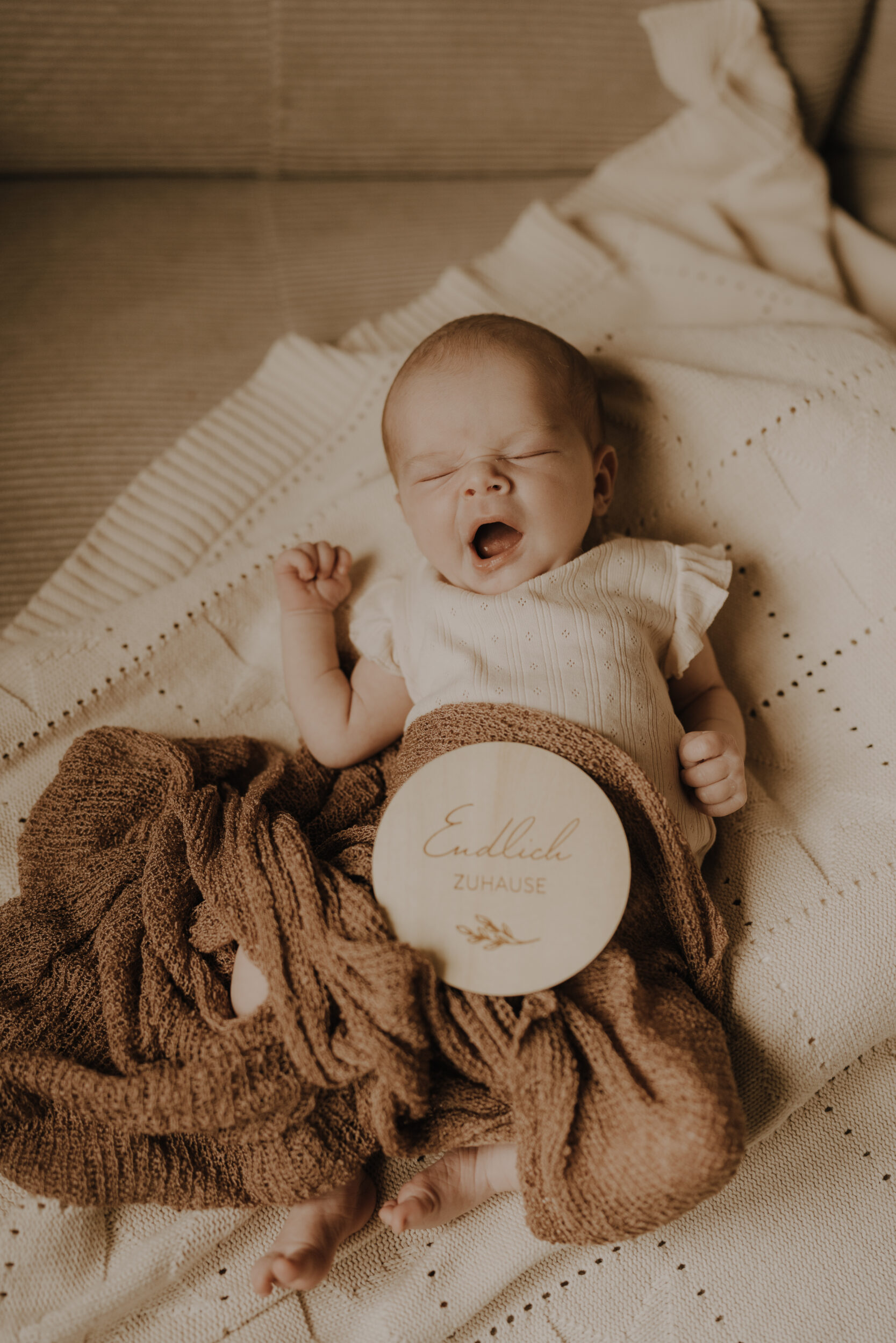 Newborn Portfolio gähnendes Baby unter brauner Decke und Schild: Endlich zu Hause