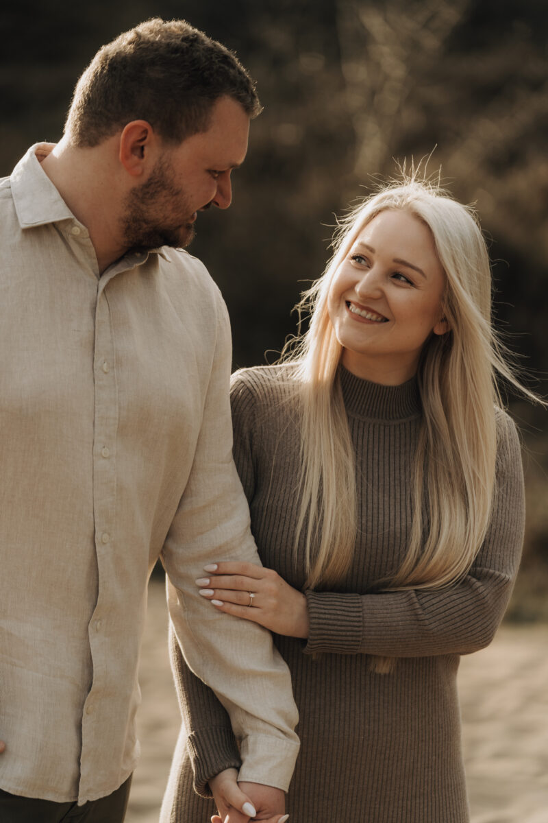 Paar schlendert Händchen haltend über eine Wiese und lächelt sich an