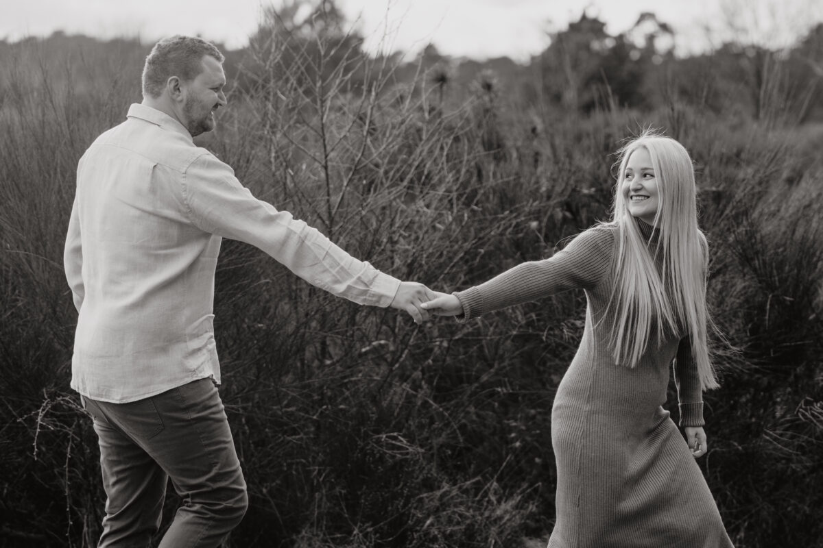 Paar läuft Händchen haltend im Sand und schaut sich an, fotografiert in Schwarz -Weiß