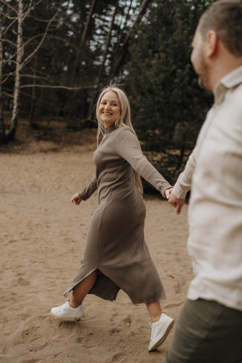 Paar schlendert durch den Sand, sie schaut zurück in die Kamera