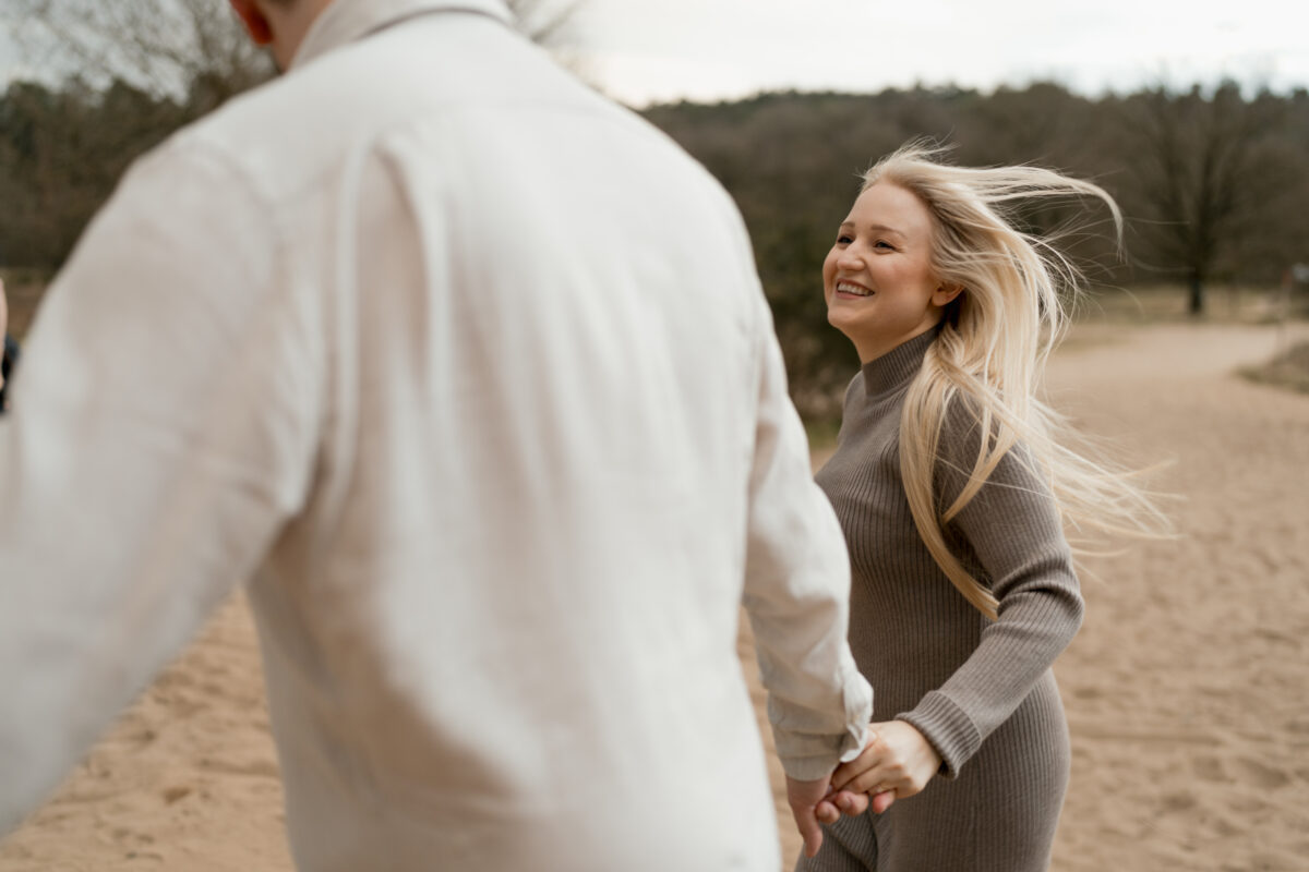 Paar läuft Händchen haltend durch den Sand und lacht