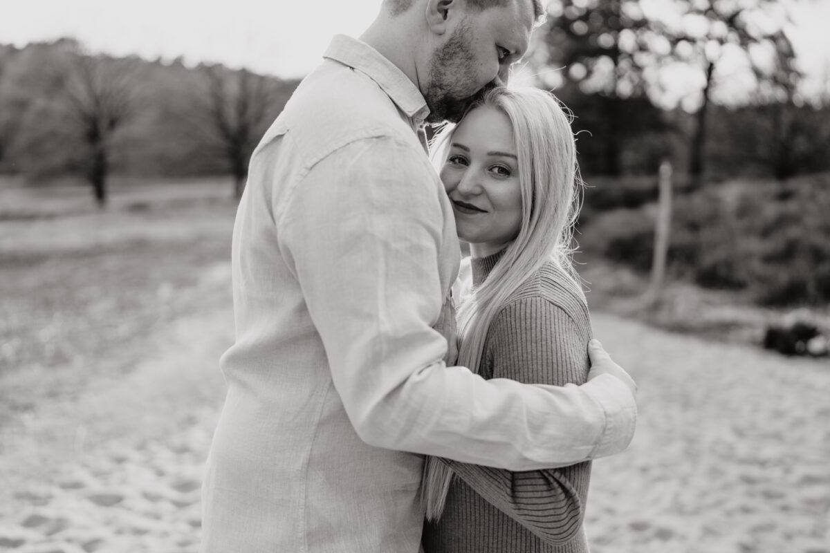 Er küsst ihren Kopf, sie schaut in die Kamera und lächelt, fotografiert in Schwarz-Weiß