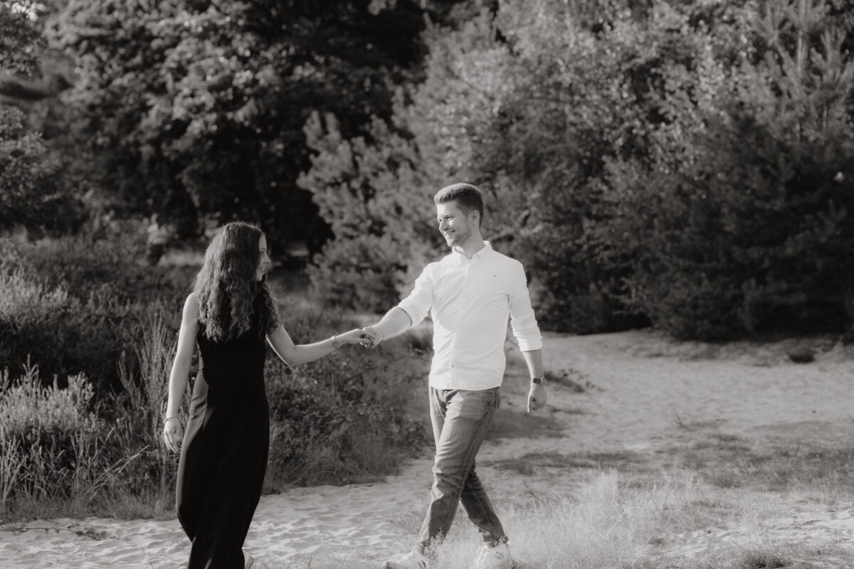 Paar schlendert Händchen haltend über eine Wiese, fotografiert in Schwarz-Weiß