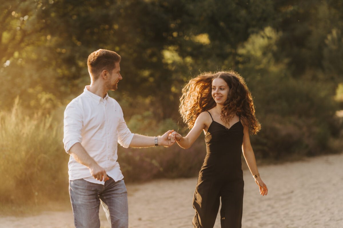 Paar läuft Händchen haltend im Sand und schaut sich an