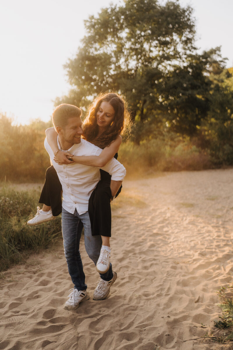 Paar läuft Huckepack in der Abendsonne auf die Kamera zu