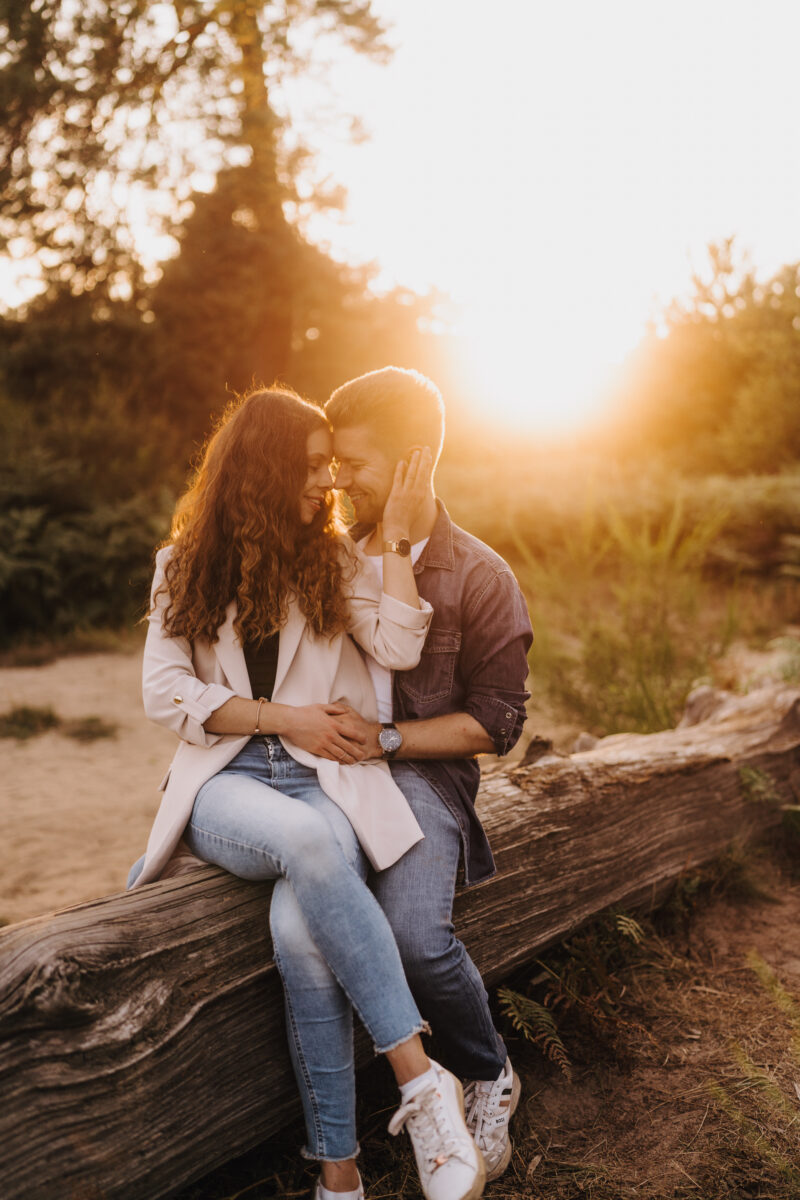 Paar sitzt Arm in Arm auf einem Baumstamm im Sonnenuntergang