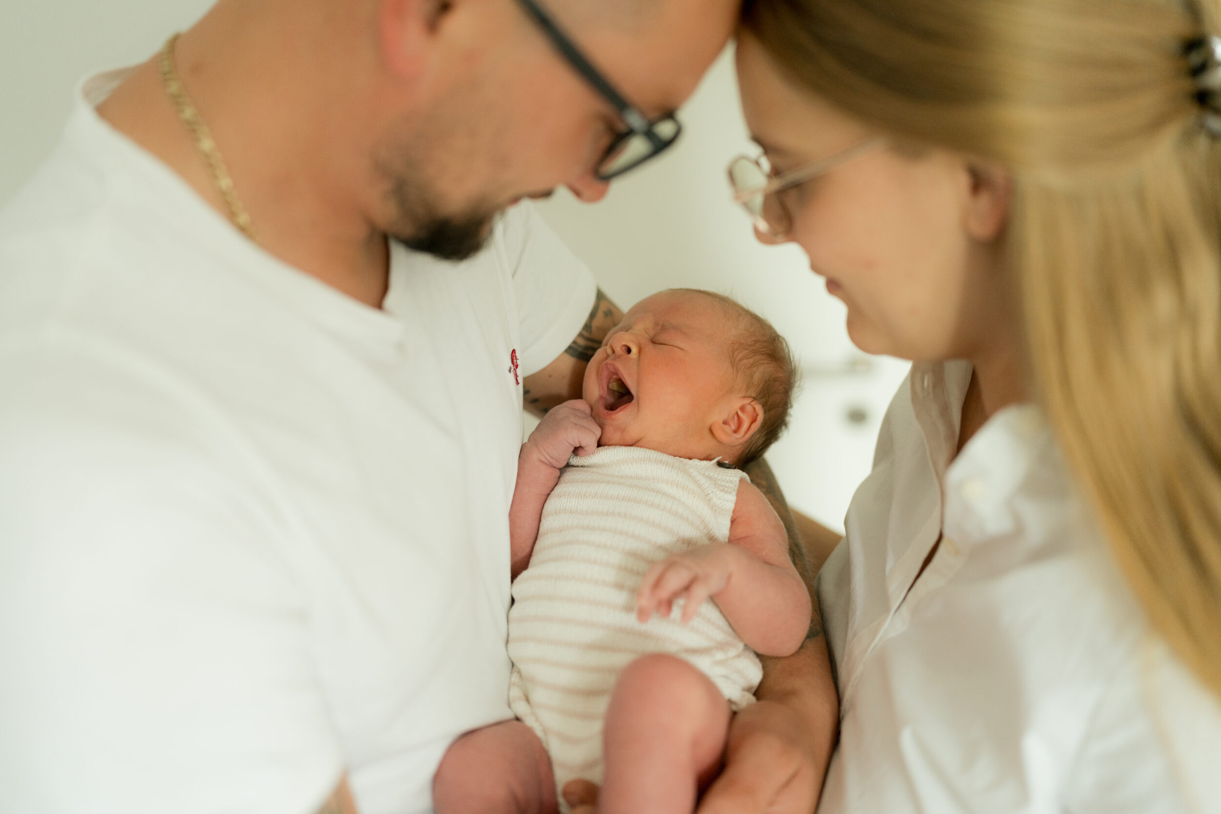 Newborn Portfolio Gähnendes Baby Newborn in Mamas und Papas Arm
