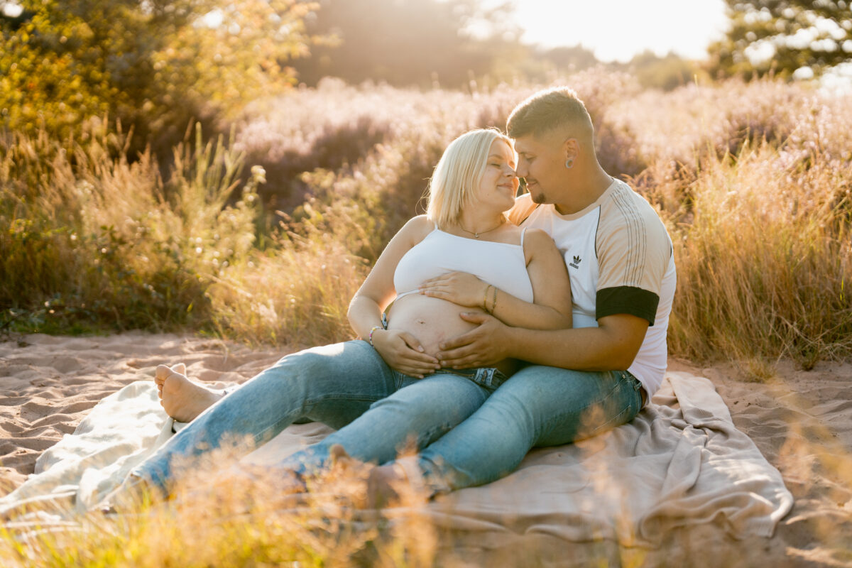 Babybauch Fotografie Portfolio junges Paar posiert sitzend auf einer Picknickdecke in der Natur