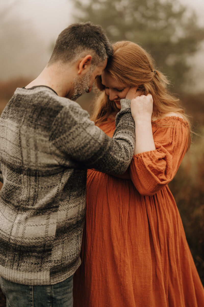 Babybauch Fotografie Portfolio Paar steht in einem Feld Frau trägt ein orangefarbenes langes Kleid