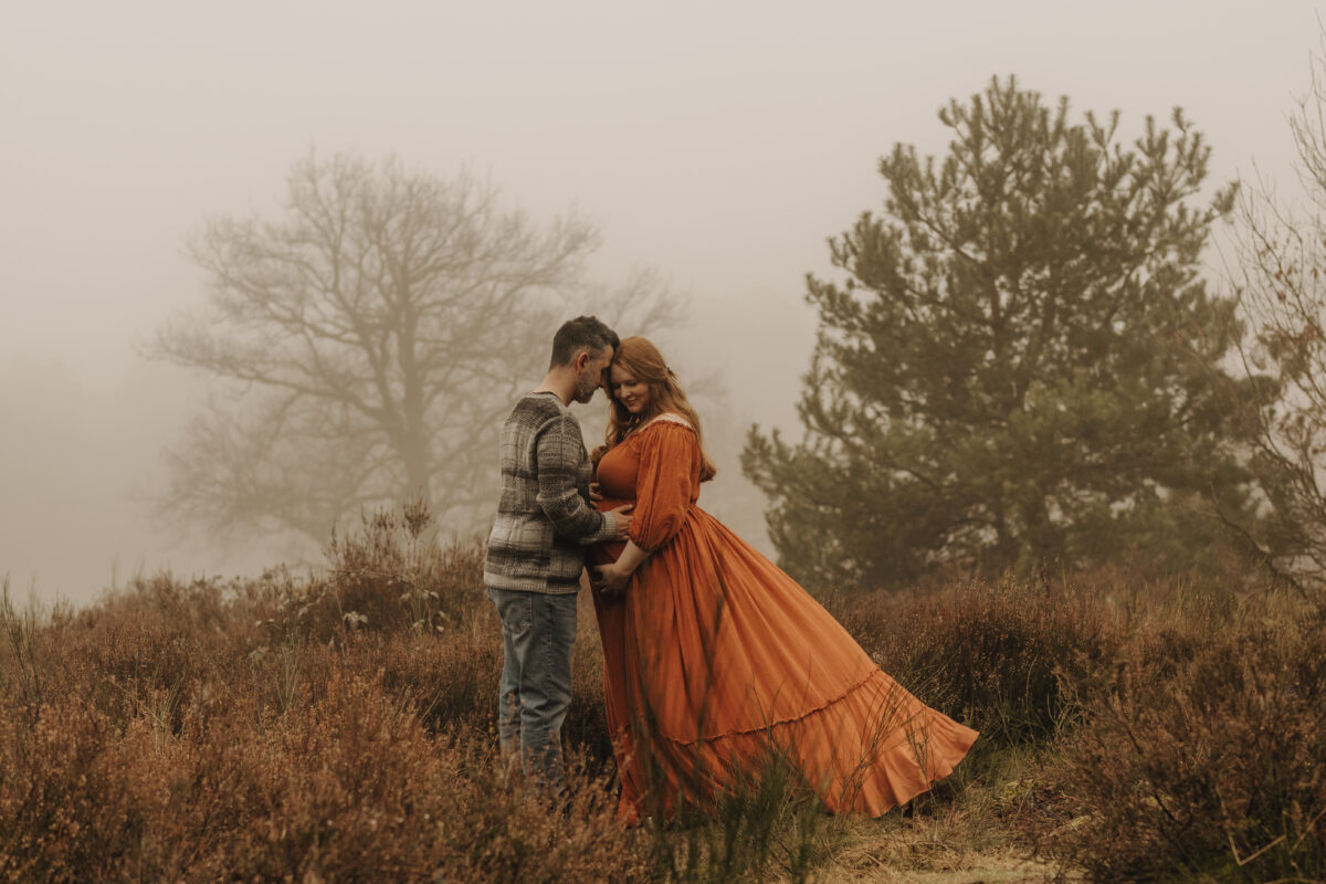 Babybauch Fotografie Portfolio Paar posiert in der Natur Frau trägt ein wehendes orangefarbenes Kleid