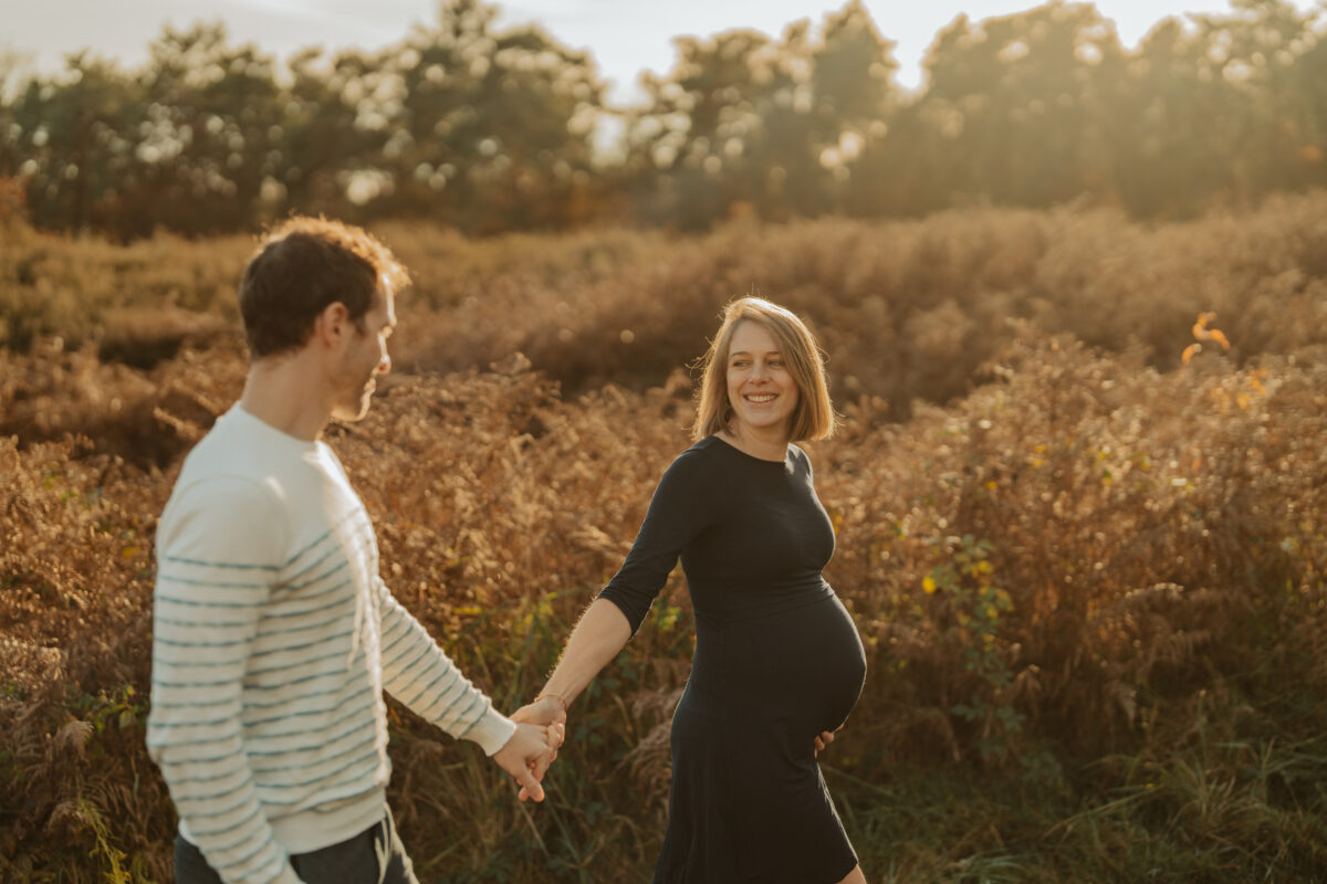 Babybauch Fotografie Portfolio glückliches junges Paar auf Feld hält sich an den Händen