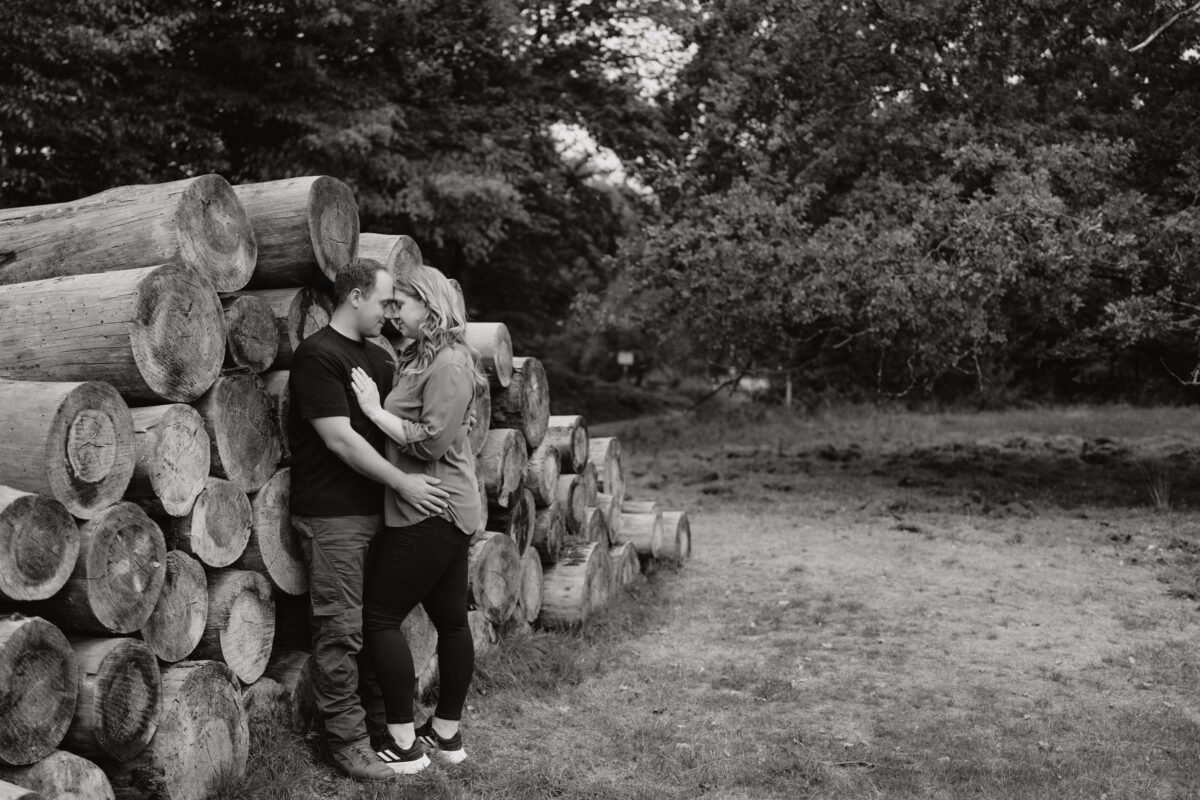 Paar lehnt sich an gestapelte Baumstämme und küsst sich