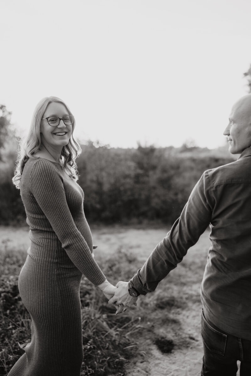 Babybauch Fotografie Portfolio junges glückliches Paar hält sich an den Händen Outdoor Schwarz-Weiß-Aufnahme