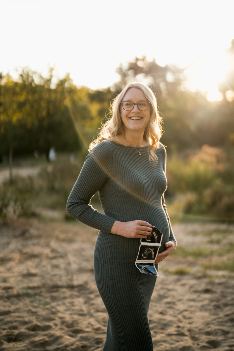 Babybauch Fotografie Portfolio schwangere Frau posiert in der Natur und hält Ultraschallbild in der Hand