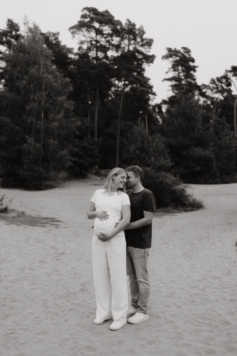 Babybauch Fotografie Portfolio glückliches junges Paar umarmt sich Outdoor Schwarz-Weiß-Fotografie