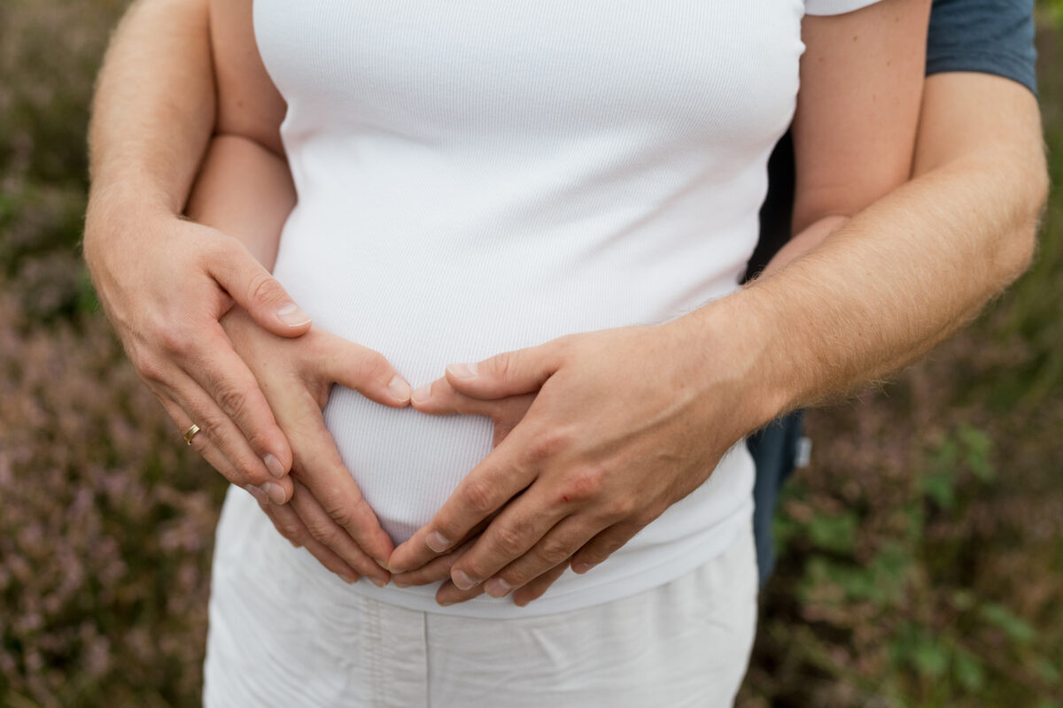 Babybauch Fotografie Portfolio Nahaufnahme vom Babybauch und den Händen der Eltern die ein Herz formen
