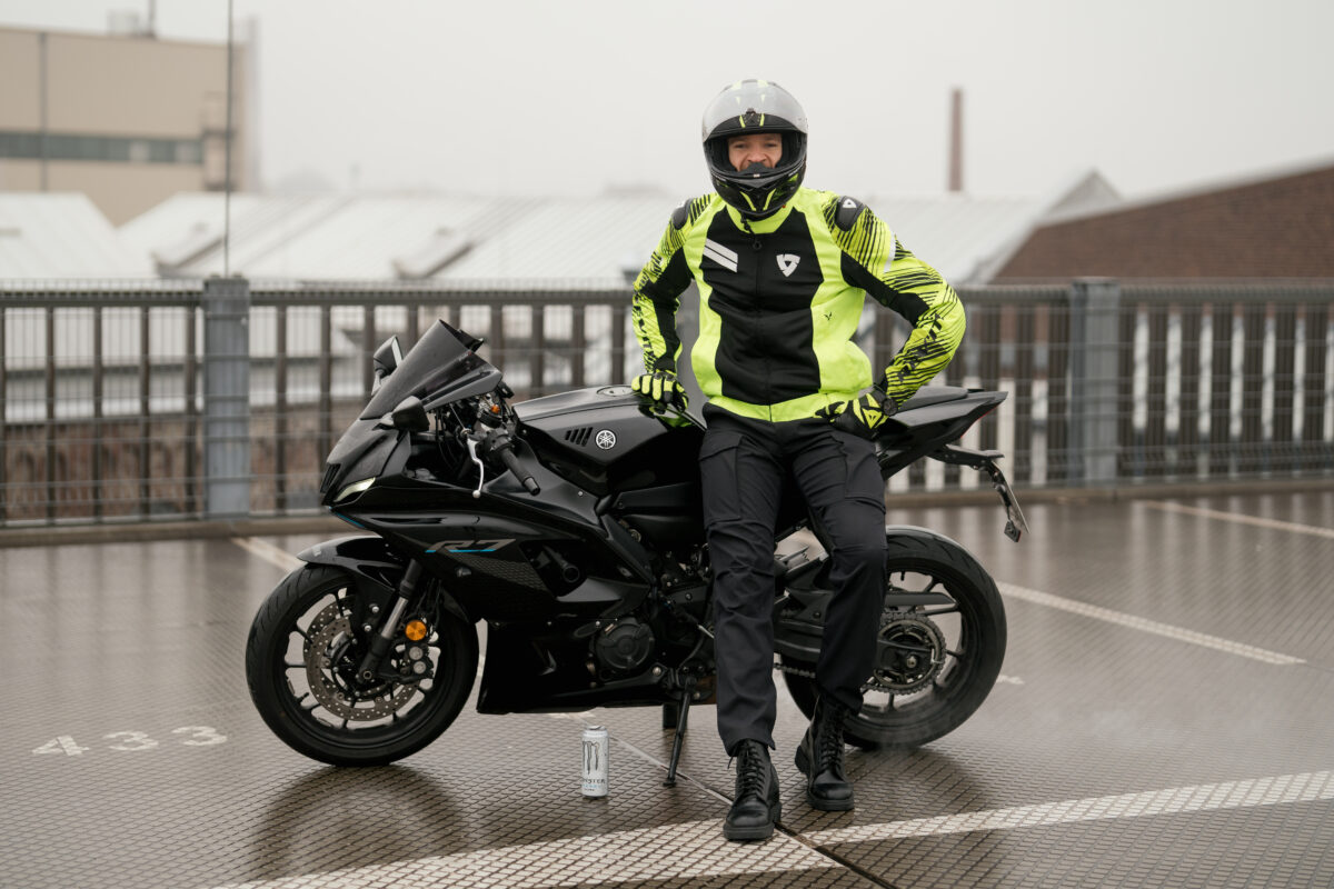 Portraitfoto eines Mannes in Motorrad Kleidung, auf ein Motorrad gelehnt