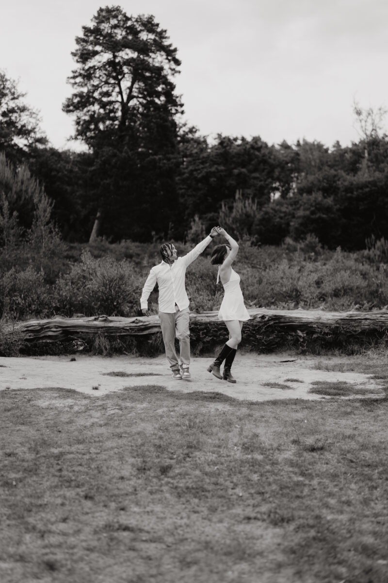 Paar tanzt fröhlich auf einer Lichtung, fotografiert in Schwarz-Weiß