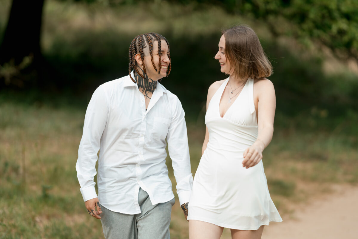 Paar schlendert Händchen haltend über eine Wiese und lächelt sich an